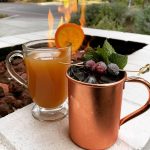 Cocktails in a copper mug and hot toddy glass on a fire pit ledge at a restaurant.