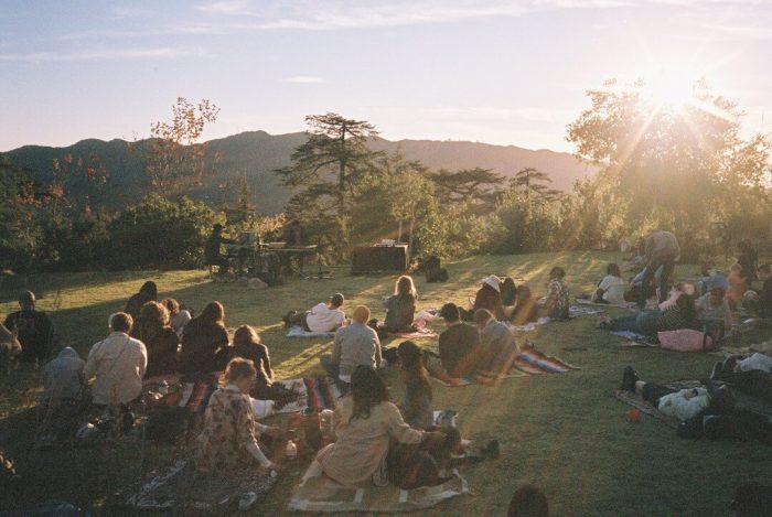 A crowd of people laying on the grass in the botanic gardens listening to a live band of two keyboard players at an autumn event.
