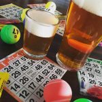Two glasses of craft beer and some bingo cards and colorful bingo balls at a brewery.