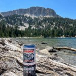 A can of craft beer on a rock with a mountain and a lake in the background.