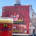 A glass of craft beer in the foreground and a hot spicy food truck in the background outside.