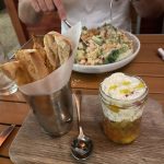 Salad in a mason jar with bread sticks and a chicken dinner in the background being eaten by a man.