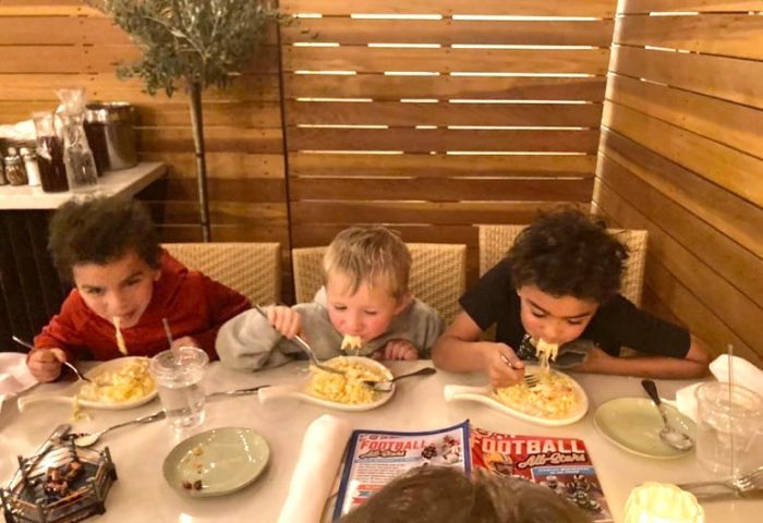 Three kids eating pasta at a restaurant for their spring break bucket list in Claremont.