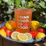 A glass with beer that says drink good do good and fruit around it.
