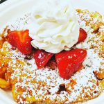 A waffle with powdered sugar, strawberries and whipped cream at Wolfe's Kitchen and Deli