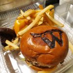 A hamburger with fries in a to go container branded with the letter W for Wolfe's Kitchen and Deli.