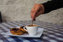 A man's hand stirs his espresso and a pastry in on the same little plate at Euro Cafe.