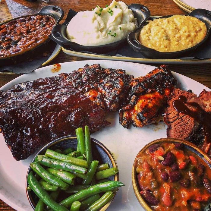 A plate of tri tip, green beans, corn, grits, potatoes, baked beans and more at a BBQ restaurant.