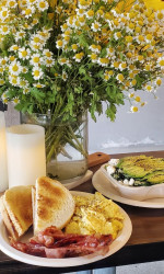 Claremont Village Eatery serves delicious breakfasts. Bacon eggs, toast, with a beautiful candle and flower on table.