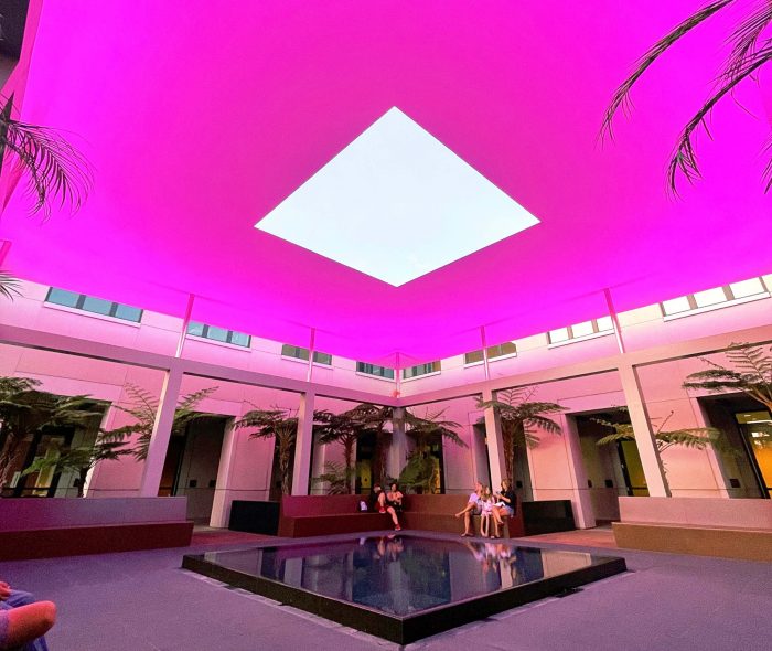 An outdoor courtyard at a college lit up by pink lights. A square cutout in the center shows the sky just before night.
