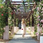 Woman in white dress walking away into a covered arbor of leaves and flowers at Scripps Womes college.