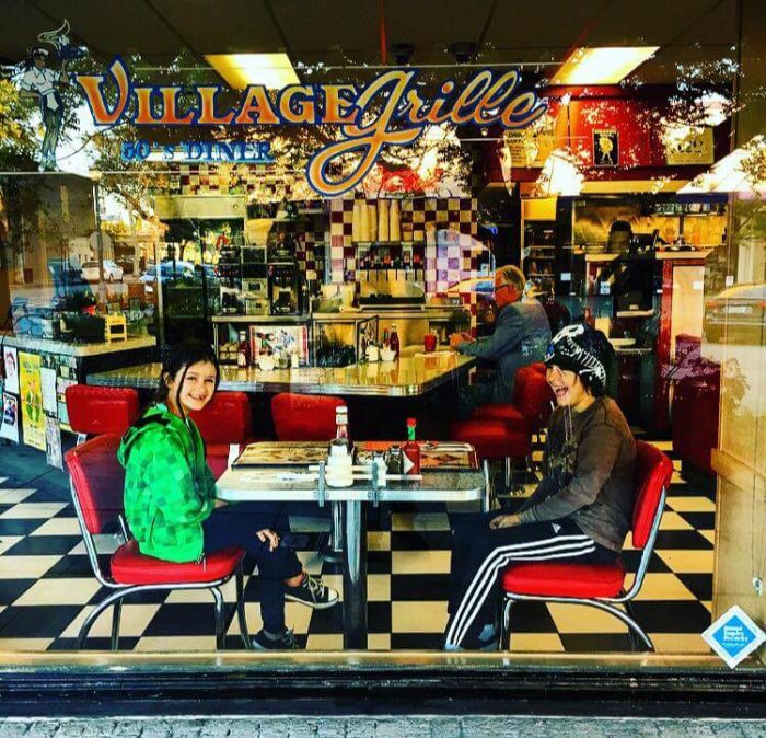 Family sitting at a table in a 50s style diner with red booth and black and white checkered floor.