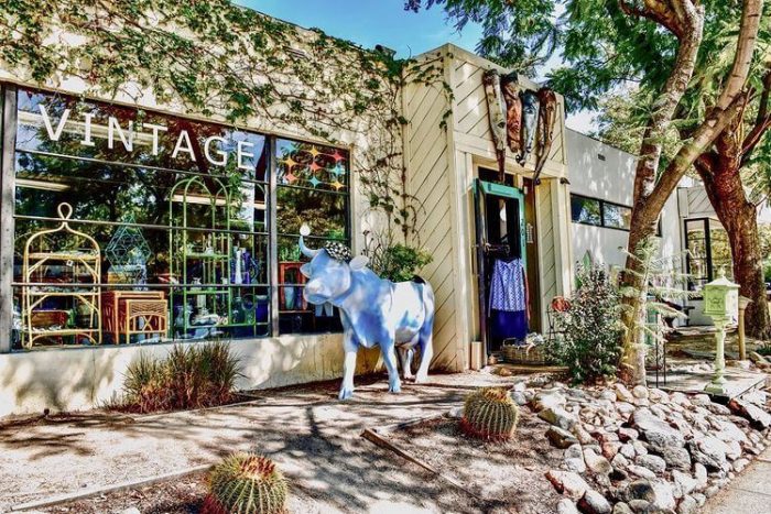 A blue cow statue is outside a building on the sidewalk and a sign says Vintage on the window. 