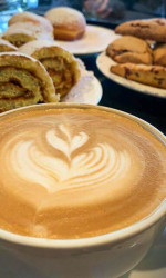 espresso coffee with heart design in foam and freshly baked pastries behind the cup.