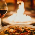 A glass of red wine and a pizza in front of a warm glowing fire at Walter's Restaurant