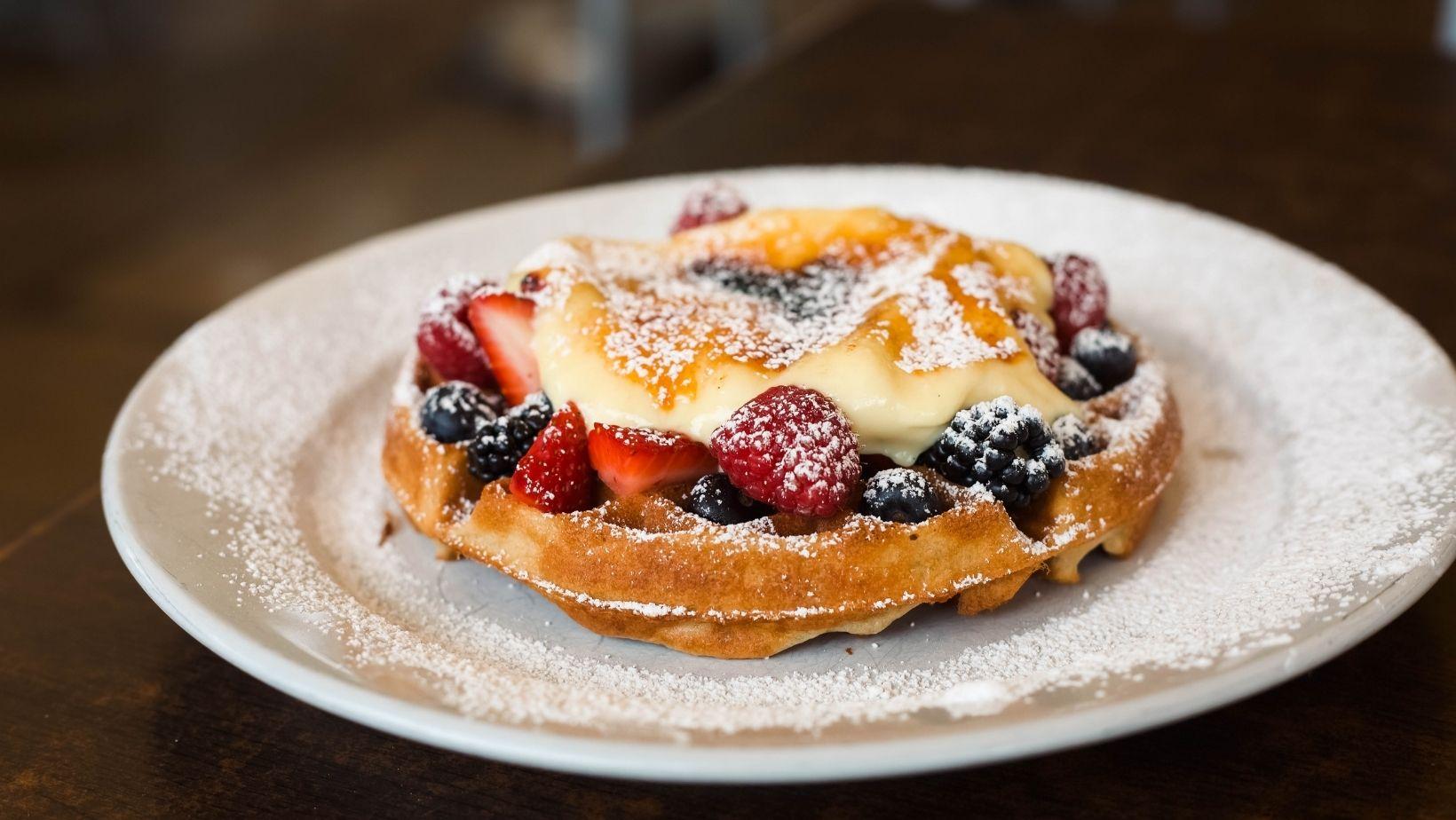 A waffle with berries and creme brulee and powdered sugar on top for brunch.
