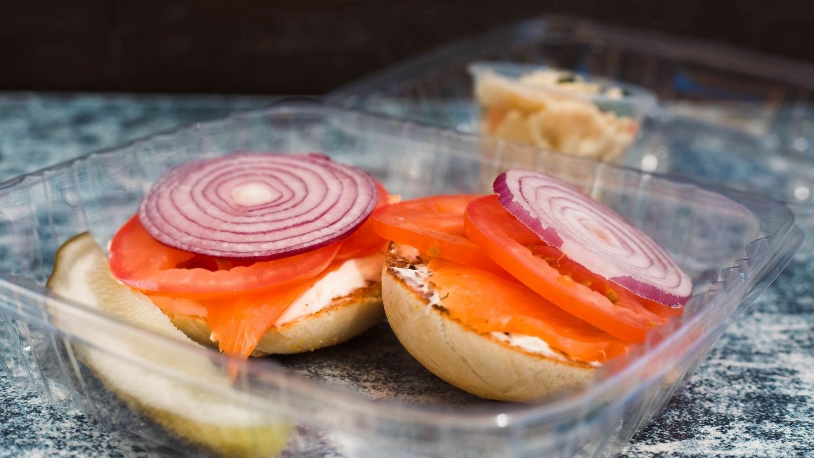 A toasted bagel with cream cheese, lox, tomato, red onion and a pickle on the side. 
